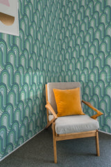 A room with a wallpaper design called Green Retro Wave, characterized by an arrangement of curved, overlapping arches in shades of green and white. The pattern has a distinctly vintage, mid-century style that adds a sense of depth and movement to the walls. A wooden armchair with a mustard-yellow cushion is placed in the foreground, complementing the vibrant background. Traditional wallpaper.