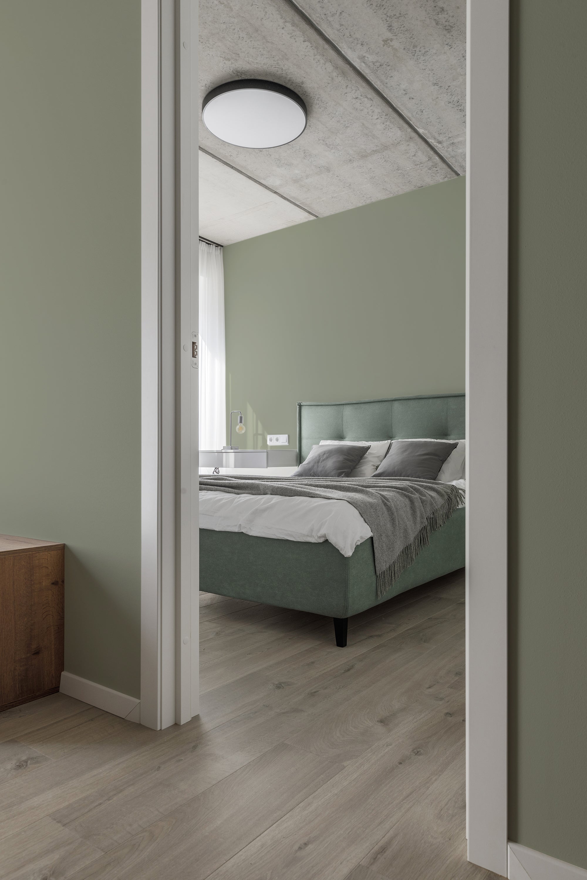 A serene bedroom with walls covered in a Solid Sage wallpaper, giving the room a calm and soothing atmosphere. The light green shade complements the minimalist d��cor and wooden flooring, creating a balanced and harmonious space. Traditional wallpaper.