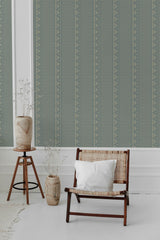 A room with a chair and plant, the wall is covered in green geometric-patterned traditional wallpaper.