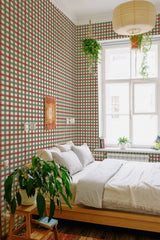 A cozy bedroom with walls covered in Autumn plaid wallpaper with red, green, and cream-colored tartan patterns, complementing the wooden furniture and indoor plants, traditional wallpaper.