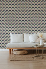 A room with a sofa in front of a wall covered in wallpaper with a geometric pattern in autumnal hues of blue, brown, and cream. The design creates a warm, modern vibe with a nod to traditional wallpaper.