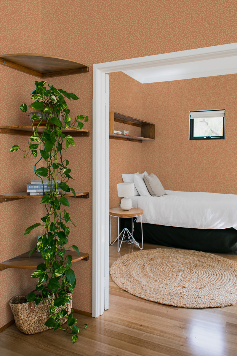 A room with terracotta-toned wallpaper patterned with delicate autumn branches, complementing the natural wood shelving and green indoor plant, traditional wallpaper.