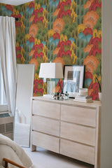 Vivid wallpaper with an autumnal forest pattern, including trees with red, orange, and yellow leaves, against a beige dresser with a mirror and lamp, enhancing the room with a traditional wallpaper touch.