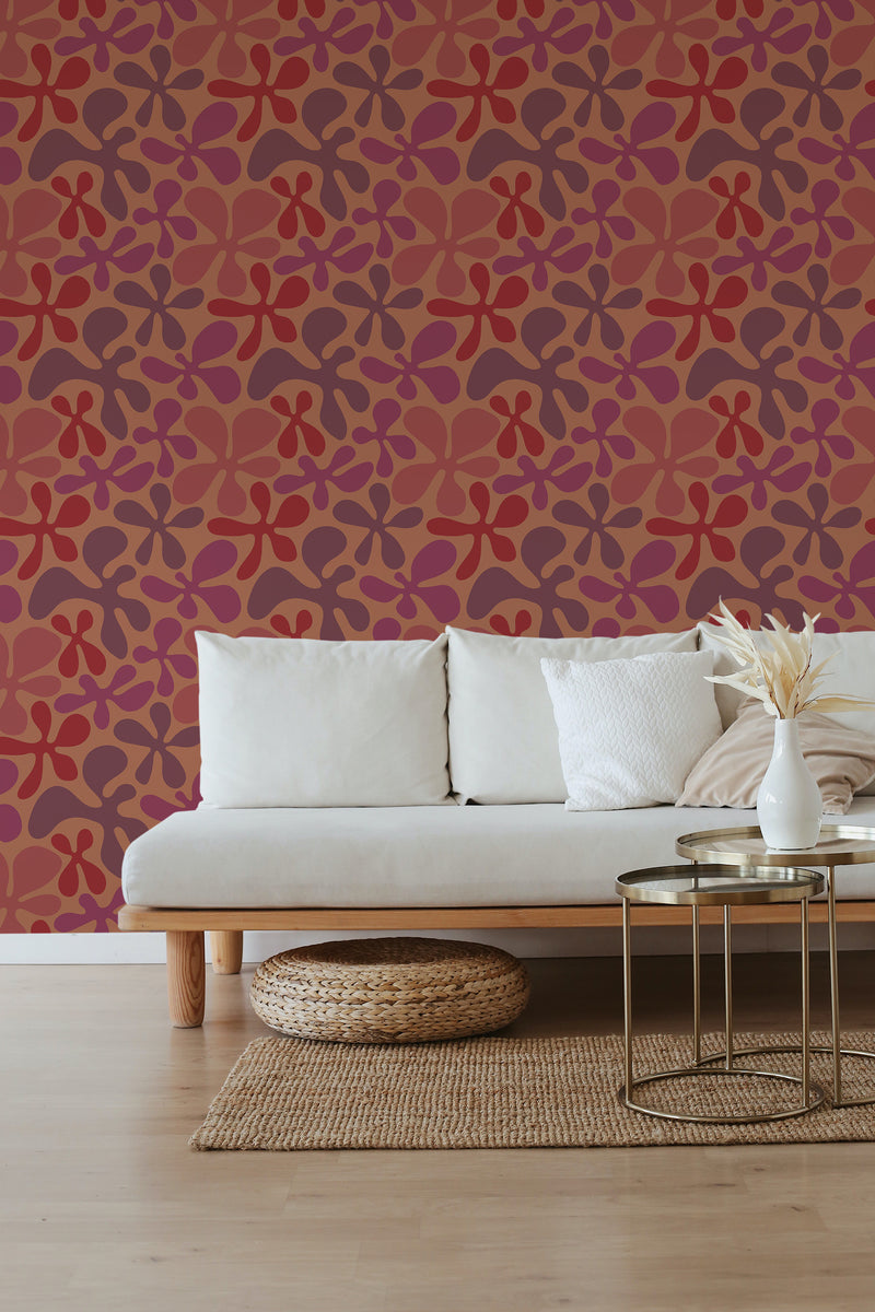 A room with a red floral wallpaper with interlocking shapes on a wall behind a beige sofa, with a natural weave rug and a small metal table in front, traditional wallpaper.