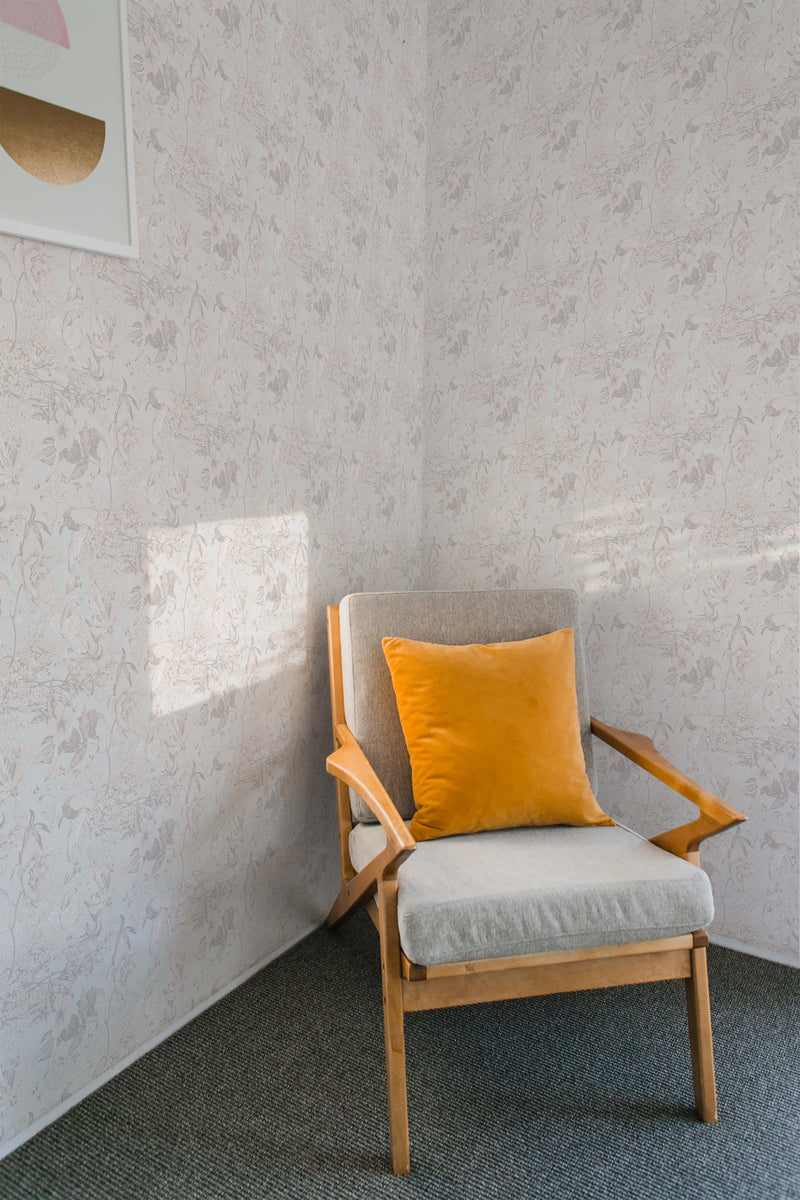 A room with light-toned floral wallpaper, adding a subtle, elegant pattern to the space. A wooden armchair with a yellow cushion complements the traditional wallpaper.