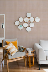 A warm-toned room with a wall covered in beige faux tweed fabric wallpaper, complemented by modern furniture and decorative round mirrors, creating a cozy ambiance with traditional wallpaper.