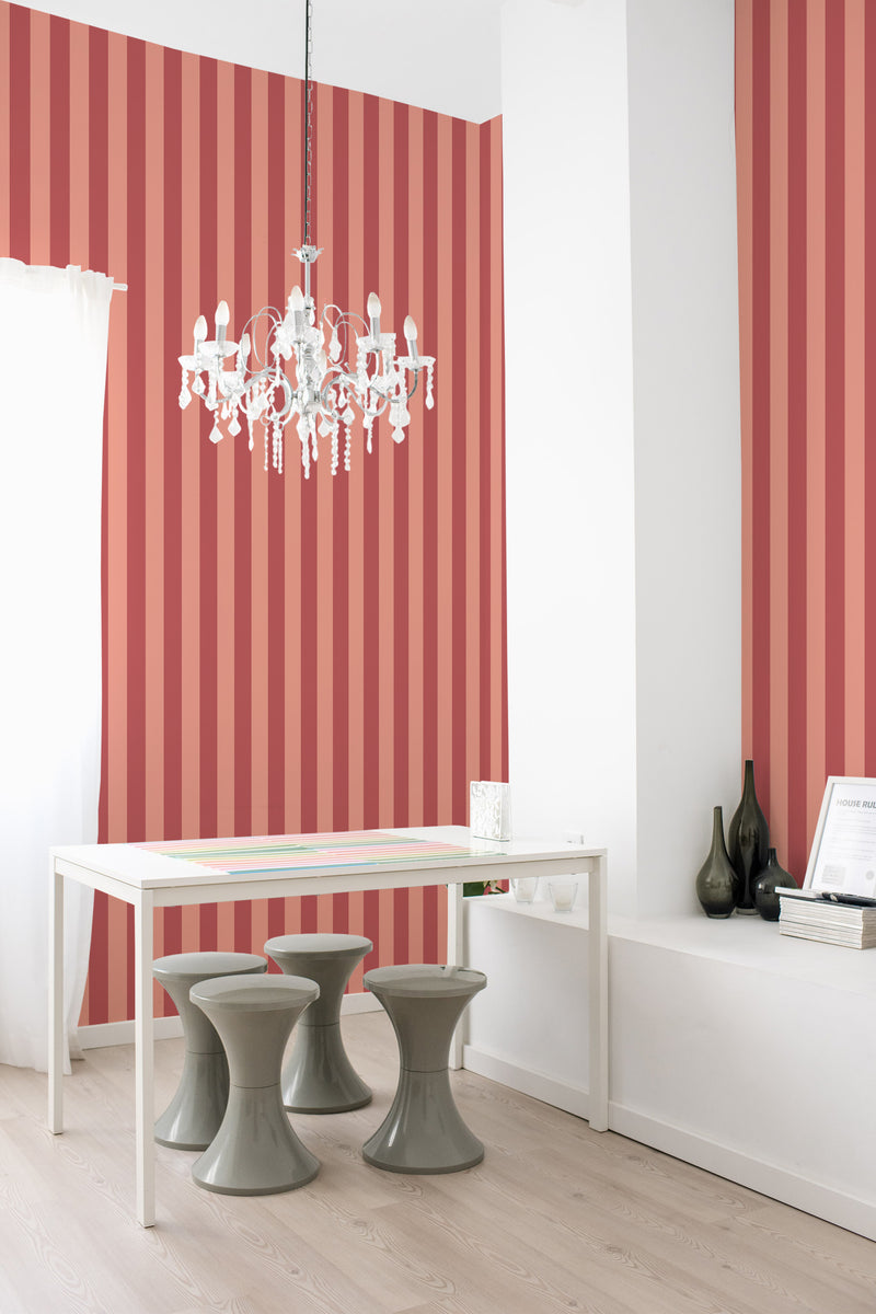 A room with pink and red striped traditional wallpaper on the wall, complemented by a white desk and modern stools.