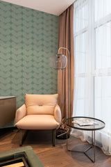 A room with a wall adorned in Green Aesthetic Leaves wallpaper with a repeating pattern of stylized green leaves, complemented by a beige armchair, sheer curtains, and traditional wallpaper.