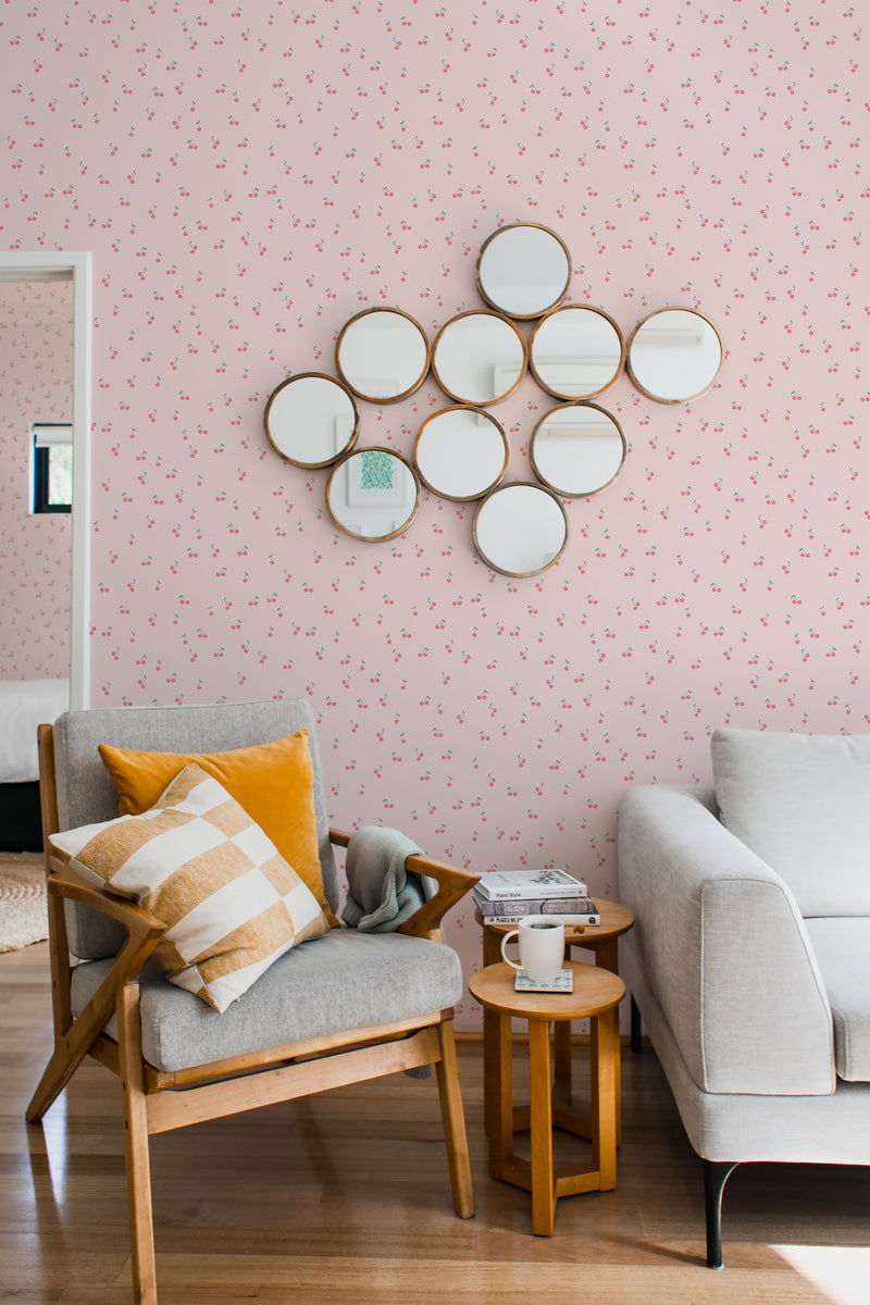 A cozy room with walls covered in a Girly cherries wallpaper design, which includes small, evenly spaced cherries on a pale background, complemented by a cluster of round mirrors and traditional furniture, creating an inviting atmosphere with traditional wallpaper.