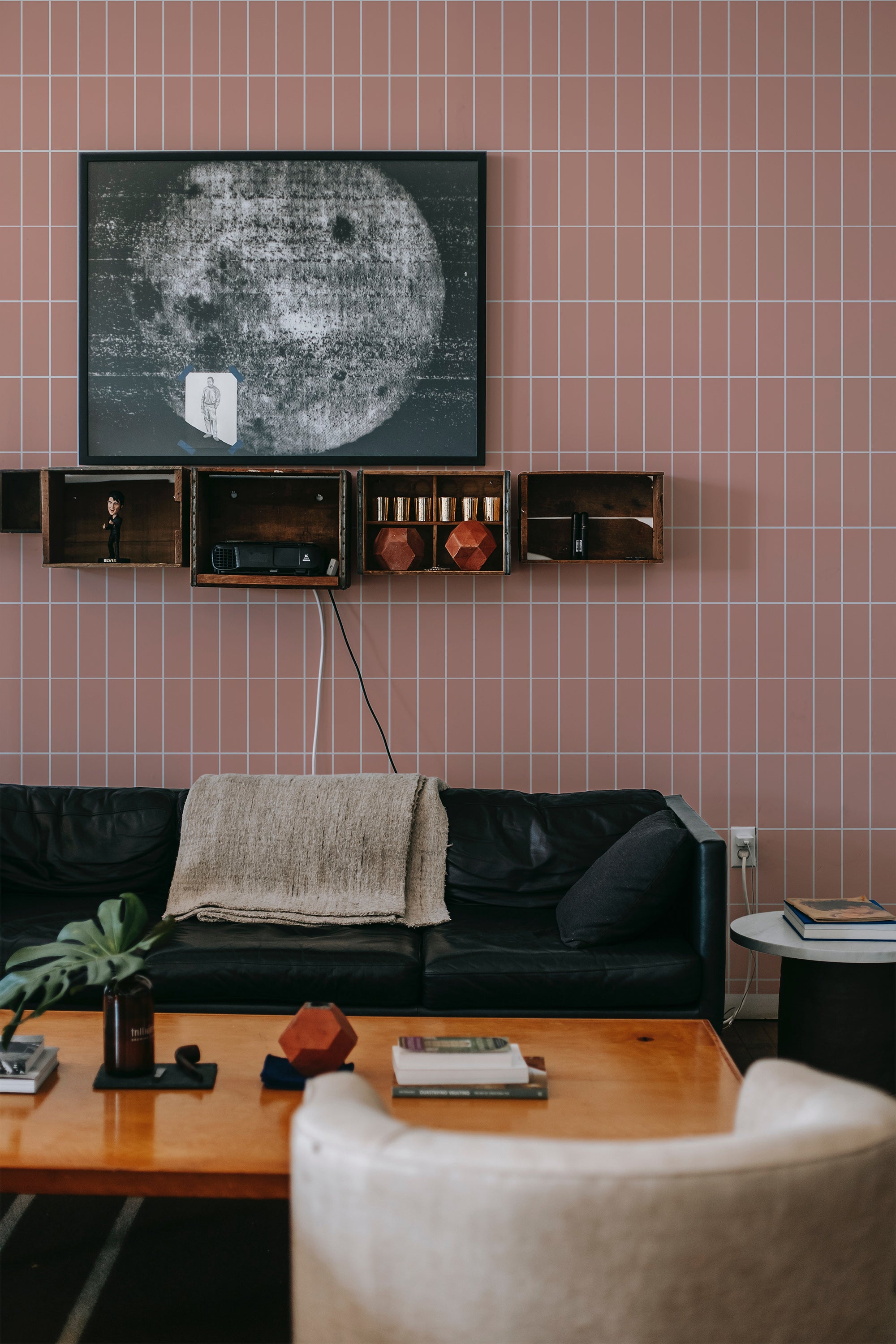 A room with pink tile-patterned wallpaper on the wall behind a black sofa and a wooden shelf with decorative items, embodying a cozy and traditional wallpaper style.