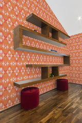 A vibrant room with walls covered in orange retro-styled circles wallpaper, complemented by a wooden shelf and two red ottomans, giving a nod to traditional wallpaper.