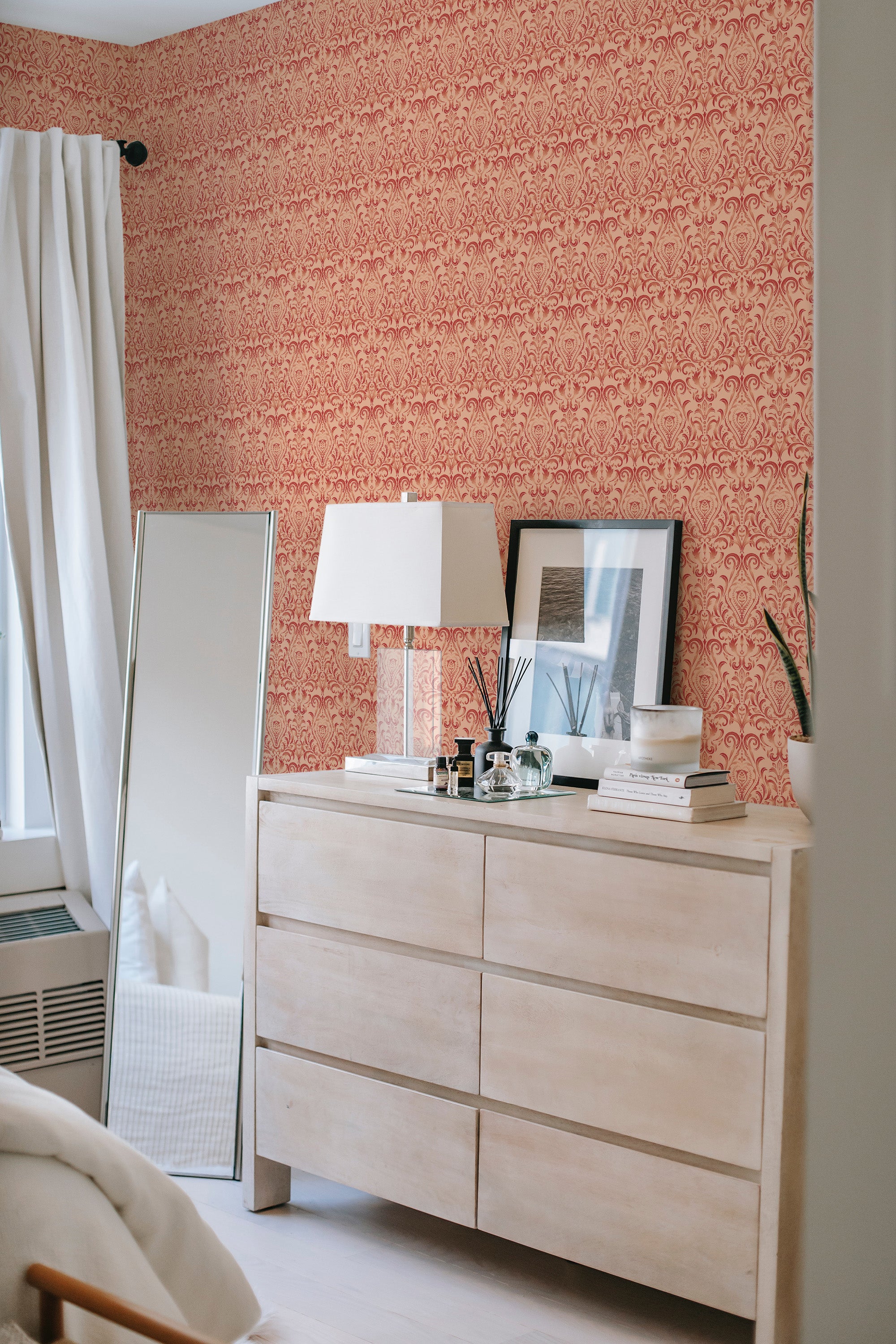 A room with peach-colored damask-patterned wallpaper covering one wall, complementing a white modern dresser and decor, embodying a traditional wallpaper.