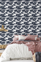 A bedroom with a wall covered in Navy Brush Strokes wallpaper, a repeated pattern of dark blue paint-like brushstrokes on a white background, giving a modern twist to traditional wallpaper.