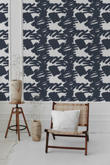 A room with a Bold Navy Stroke wallpaper design of abstract white brushstrokes on a navy background, complemented by a wooden chair and vase, embodying traditional wallpaper.