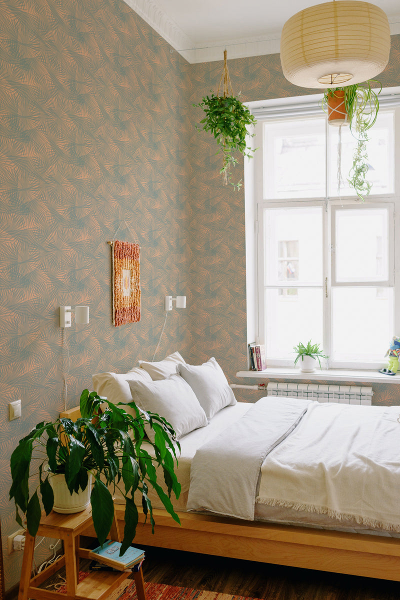 A cozy bedroom with a bed against a wall covered in Palms on Peach wallpaper with a repeating palm leaf pattern on a peach background, creating a warm and inviting space. Traditional wallpaper.