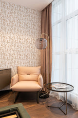 A room with walls covered in neutral floral wallpaper with delicate brown and beige flowers and vines on a light background, complementing the soft beige chair and drapes, exemplifying traditional wallpaper.