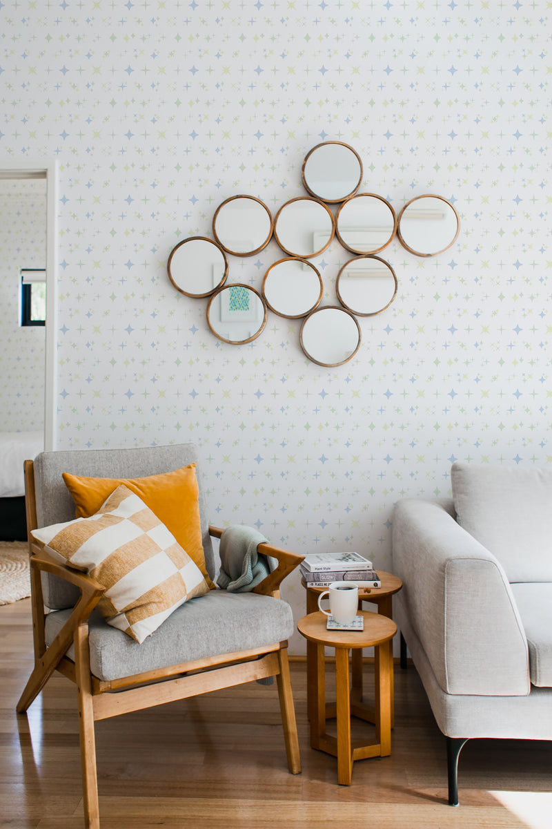 A cozy room with walls adorned by Aesthetic star-patterned wallpaper, complementing a modern chair with a throw pillow, a gray sofa, and circular decorative mirrors, traditional wallpaper.