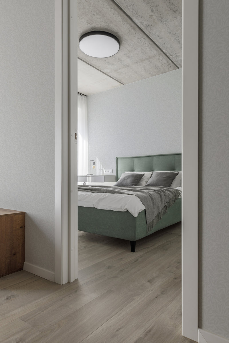 A modern bedroom with light-colored flooring and a green upholstered bed, accented by a wall covered in a subtle seamless spring leaves pattern wallpaper, invoking a calming, traditional wallpaper aesthetic.