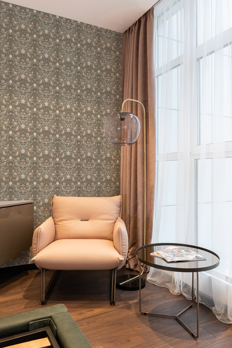 A cozy room corner with walls adorned in vintage springtime wallpaper, consisting of floral patterns in muted tones, complemented by sheer curtains and traditional wallpaper.