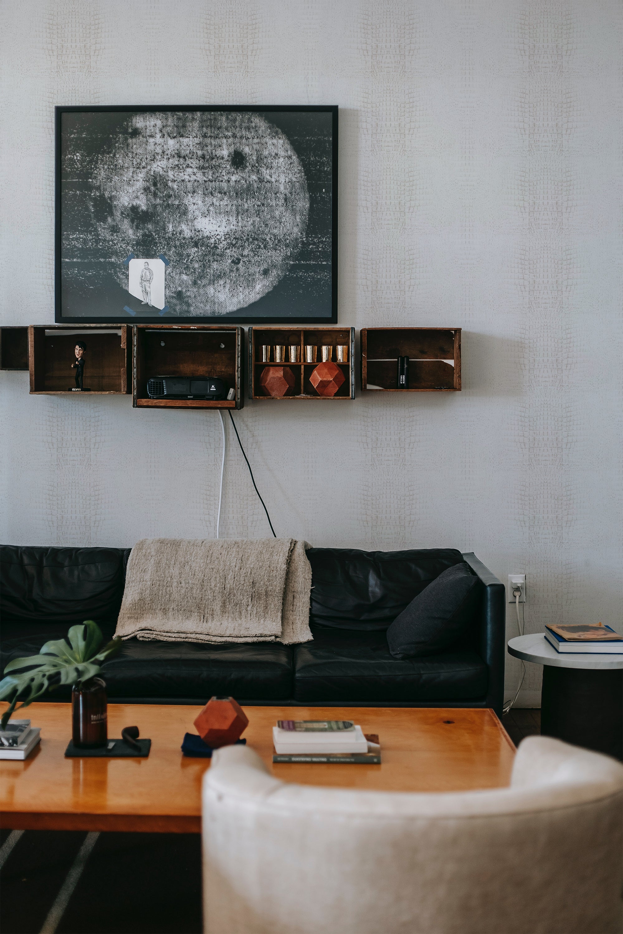 A room with light gray textured wallpaper resembling crocodile skin, complementing a modern interior with a dark sofa and wooden shelving, traditional wallpaper.