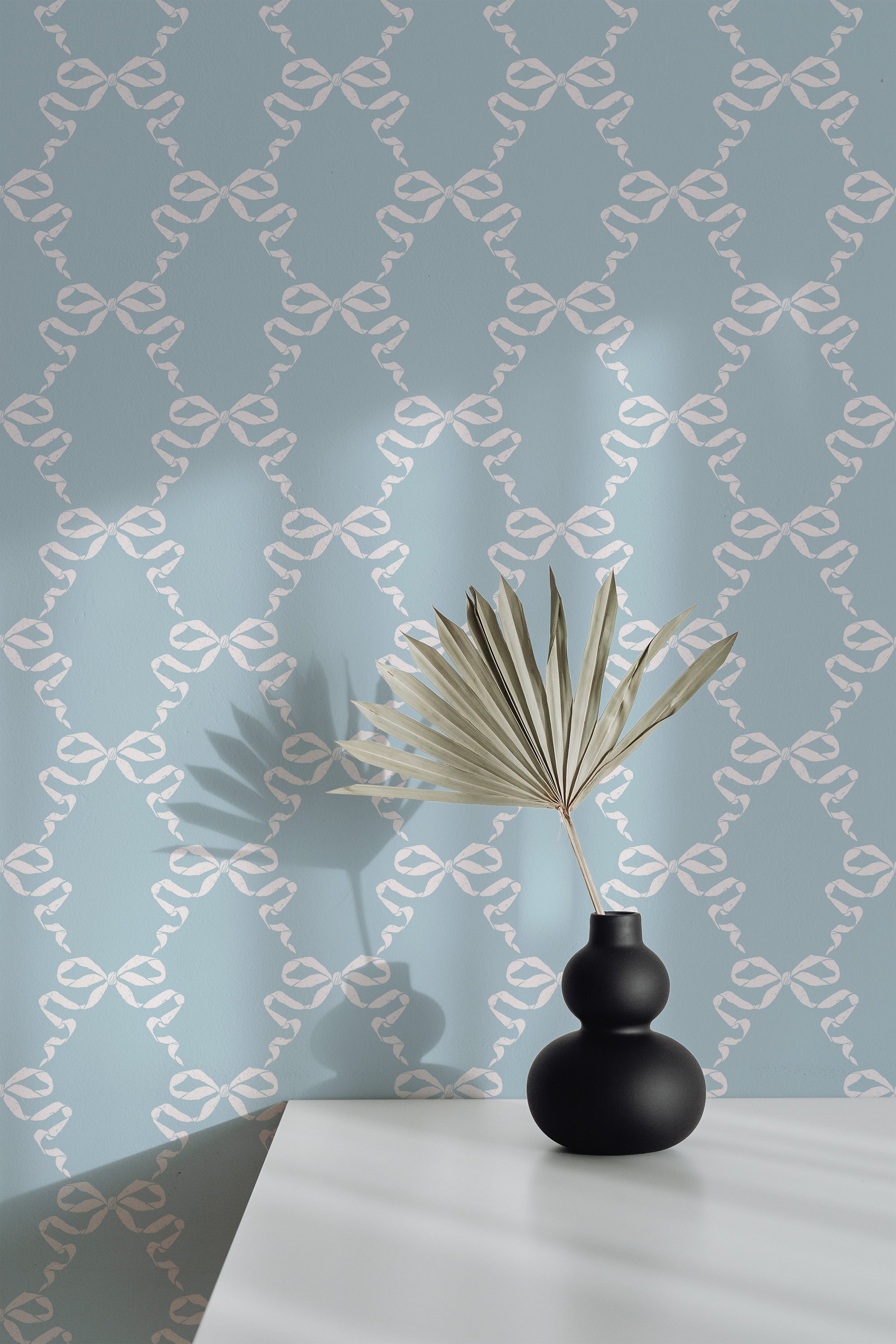 Self-adhesive wallpaper with a vintage ribbon pattern in gray and white tones on a room wall, behind a table with a black vase and decorative plant.