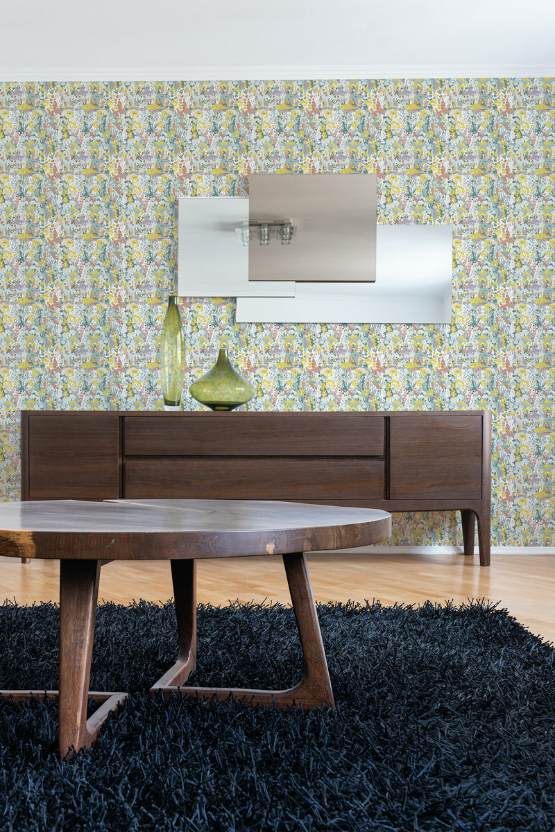 A vibrant wallpaper with a colorful abstract pattern resembling a summer meadow with various shapes and hues on a room wall, behind wooden furniture, ending with traditional wallpaper.