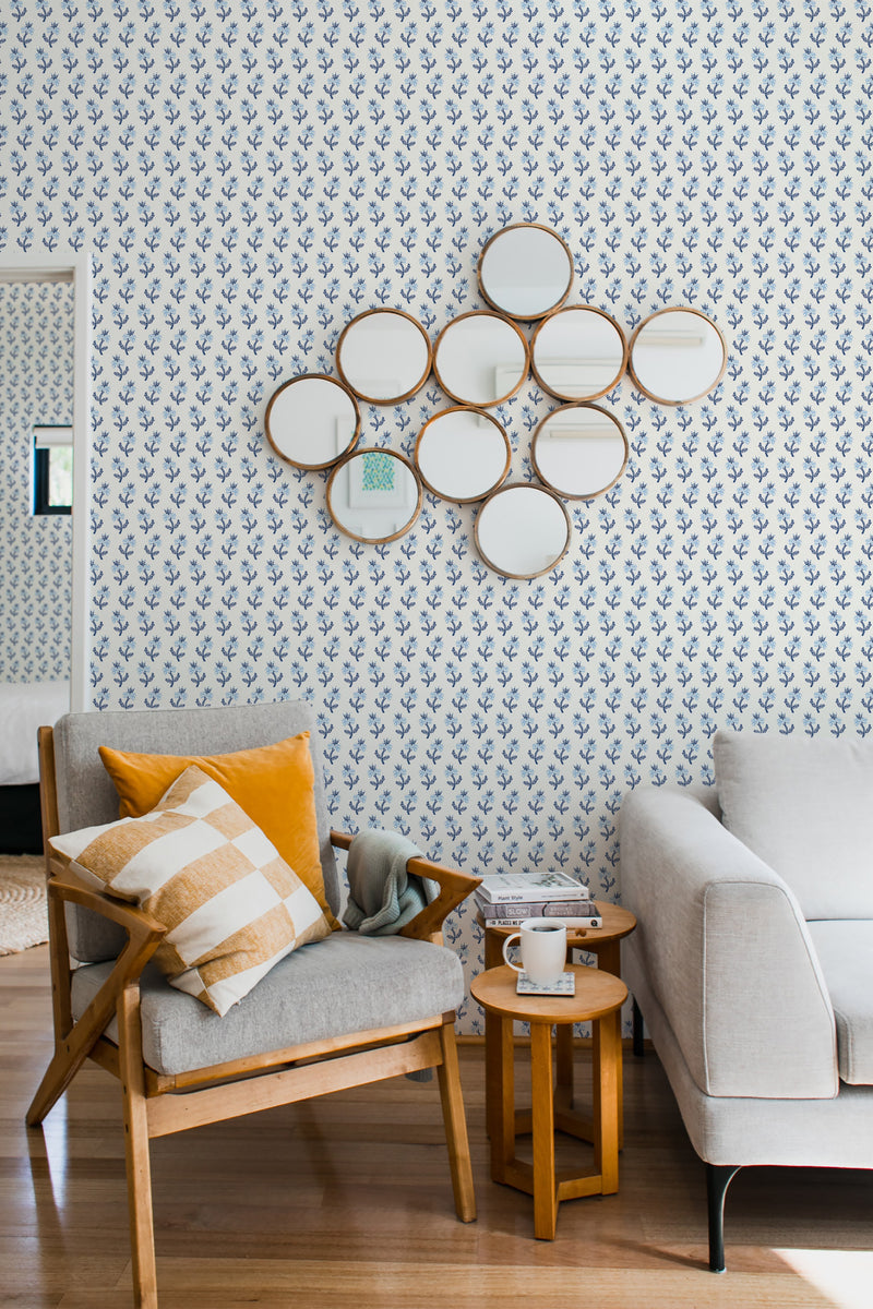 A cozy room with a wall covered in blue and white aesthetic floral pattern wallpaper, complemented by a collection of round mirrors and a sitting area with a wooden armchair, sofa, and side table,raditional wallpaper.