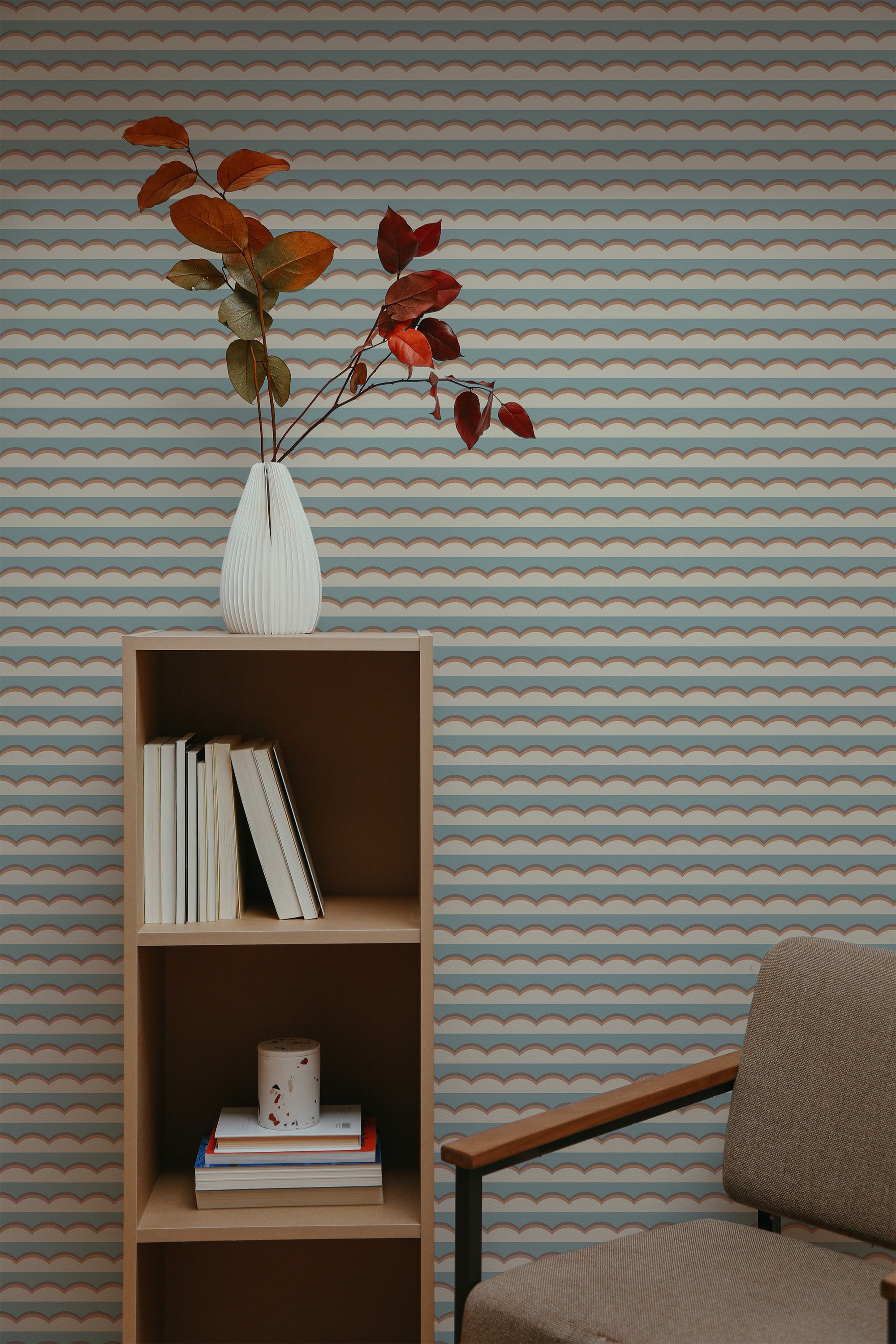 Self-adhesive wallpaper with a repeating graphic cloud pattern in pastel colors on a room wall, accented with a bookshelf and a vase with leaves.