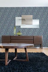 A room with a wooden sideboard and table against an Art Nouveau style wallpaper with intricate floral and curvilinear patterns in blues and greens, above a dark blue fluffy rug, traditional wallpaper.