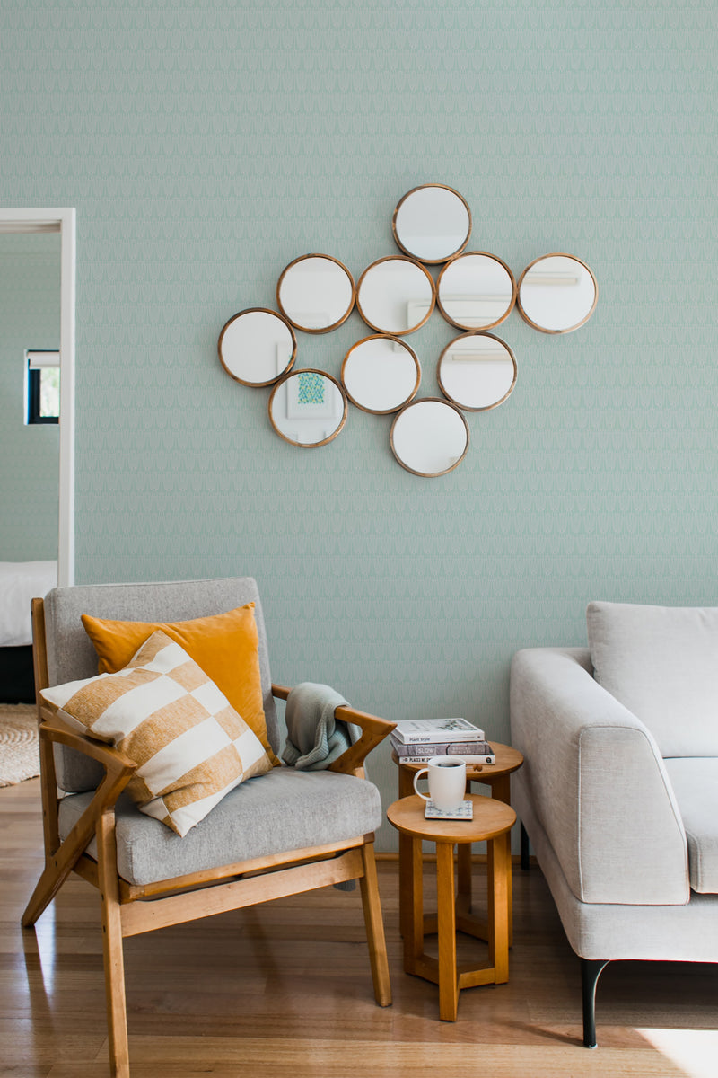 A cozy room with sage green Art Deco wallpaper displaying geometric patterns, accented by a cluster of round mirrors and furnished with modern chairs and a side table, embodying traditional wallpaper.