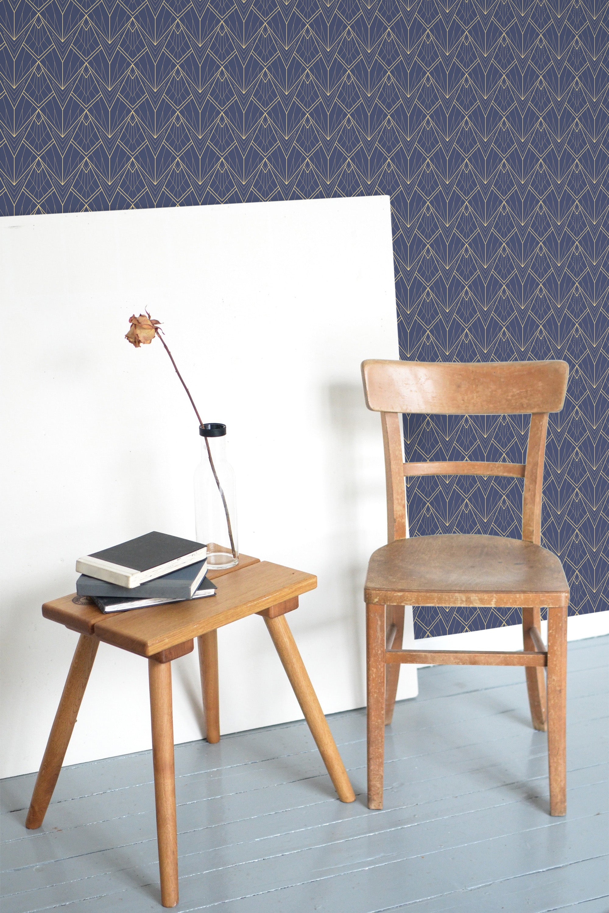 Self-adhesive Classic Art Deco wallpaper with geometric pattern in navy blue and gold, on wall above white wainscoting with wooden chair and side table.