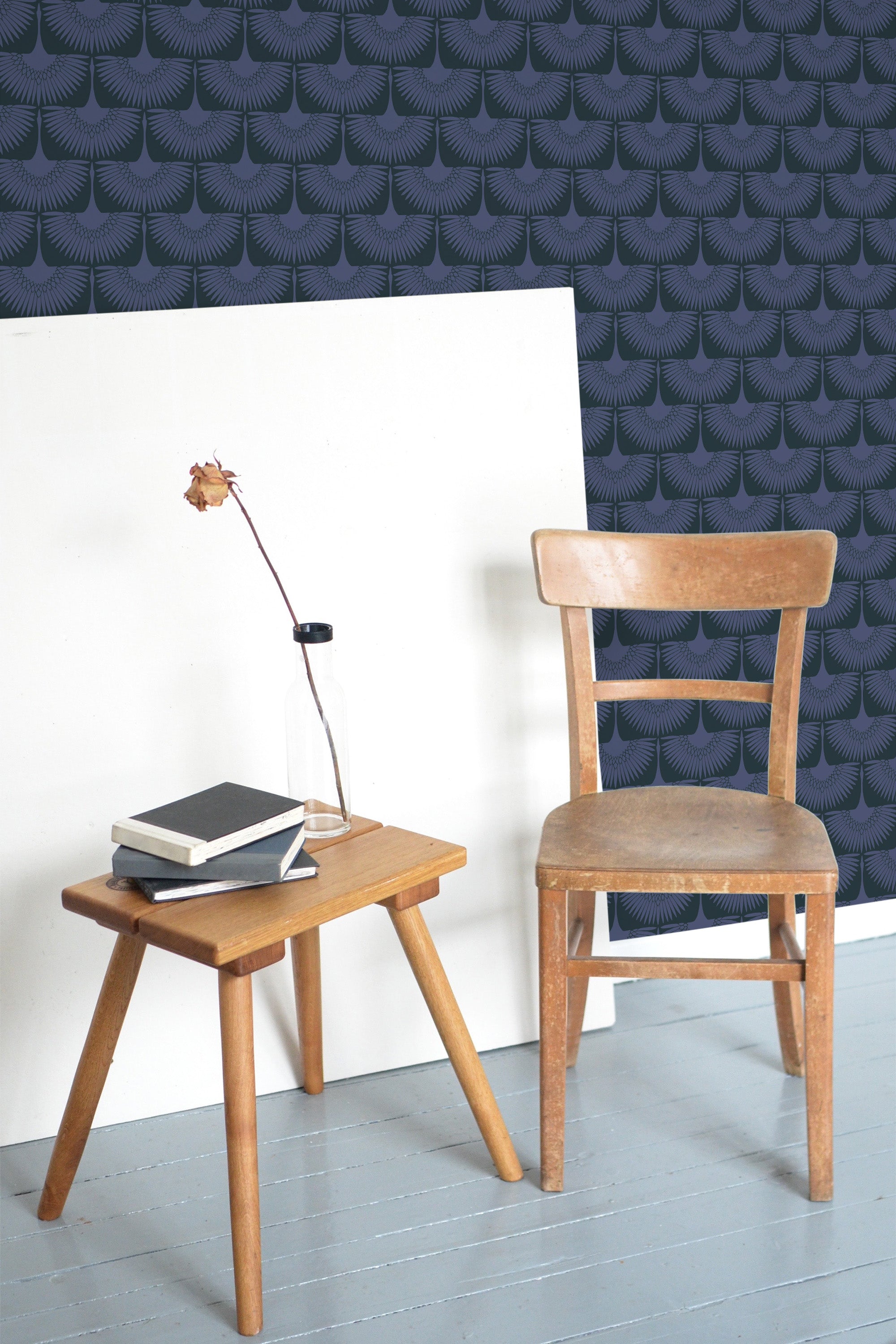 Self-adhesive wallpaper with a dark seamless swan pattern, contrasting with a light wood chair and side table in a room.
