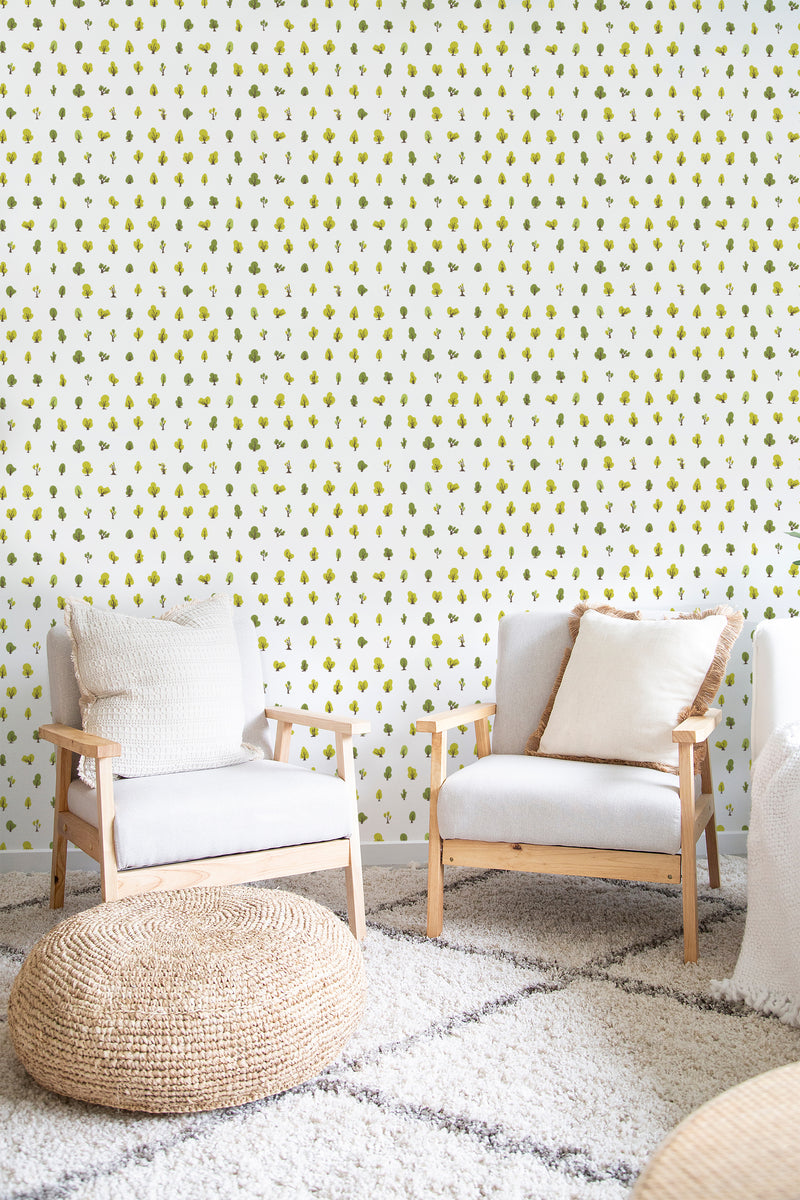 A room with Tiny Trees wallpaper design, including stylized miniature green trees on a light background, with wooden chairs and a woven ottoman, elegant and simple traditional wallpaper.