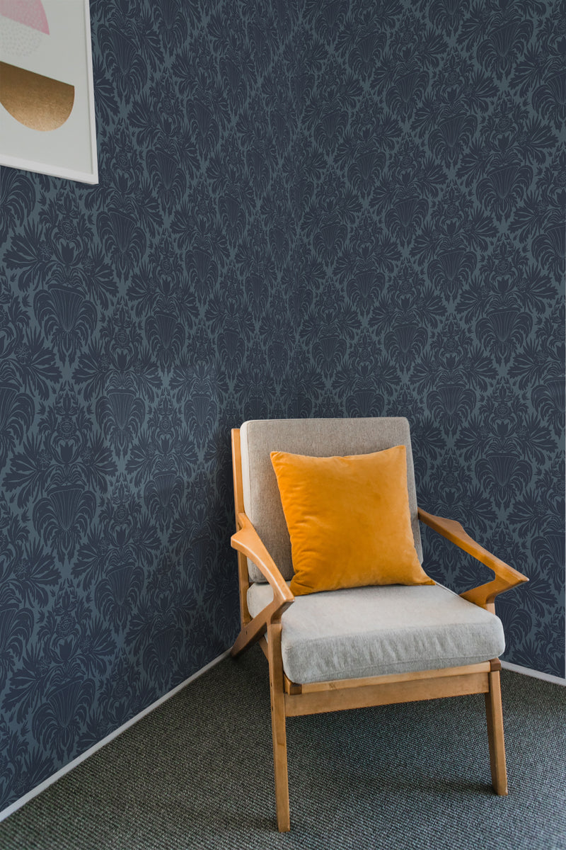 A room with an armchair against a wall covered in Classic Dark Damask wallpaper with intricate floral patterns in a darker tone-on-tone style, adding an elegant touch to the decor, traditional wallpaper.