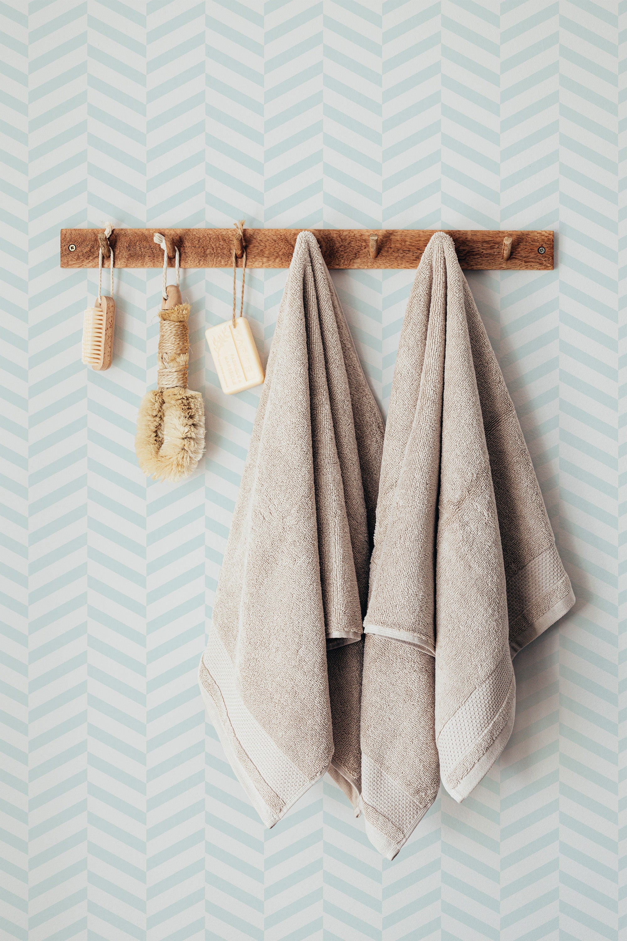 Self-adhesive Light Herringbone wallpaper with a subtle blue and white zigzag pattern, complemented by a wooden towel rack with hanging bath accessories.