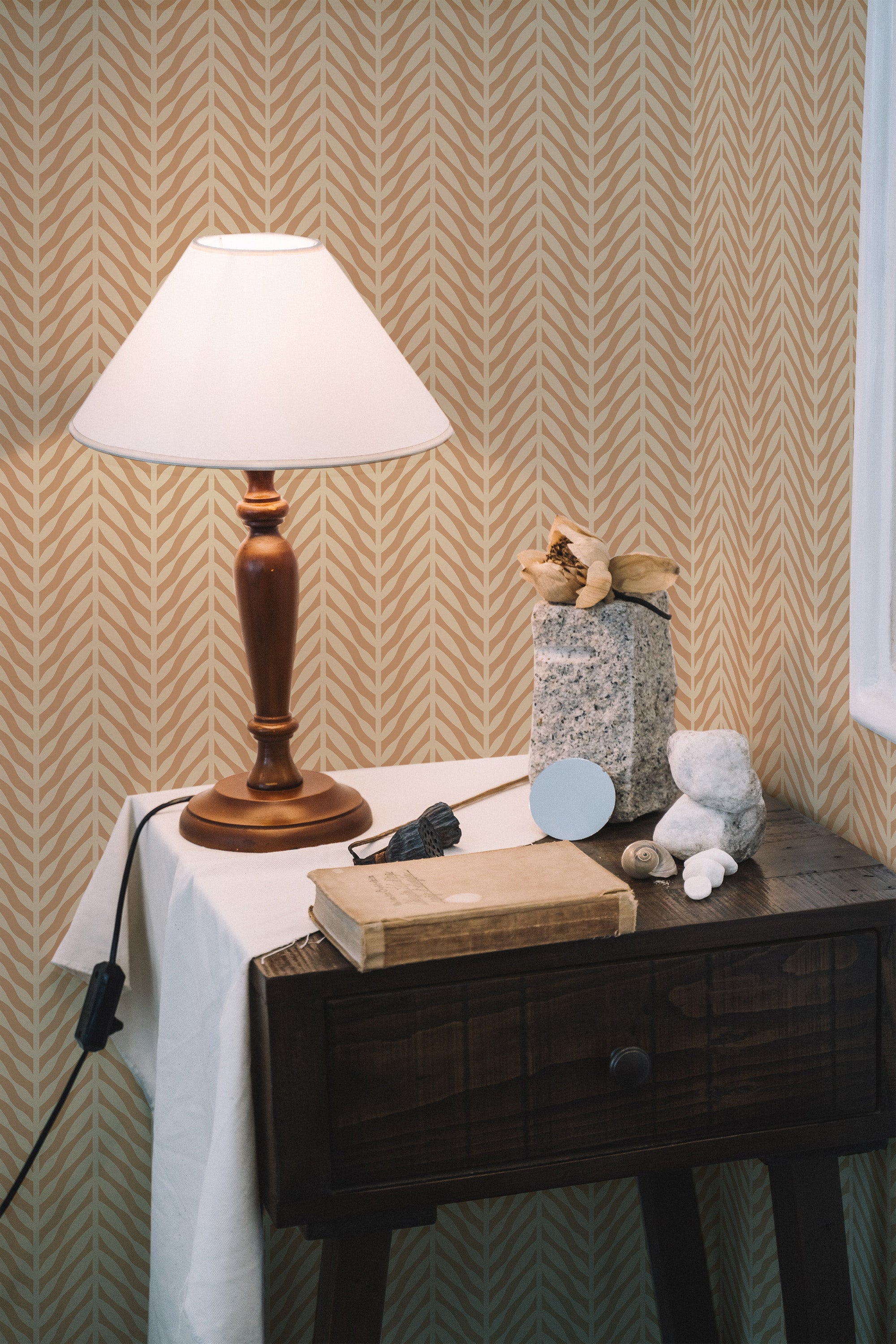 Self-adhesive Tan Herringbone wallpaper on a room wall with a wooden table, lamp, and decorative items.