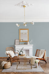 A room with pale green walls topped with a border of green and purple polka dots, above a white fireplace and between wooden accent furniture,raditional wallpaper.