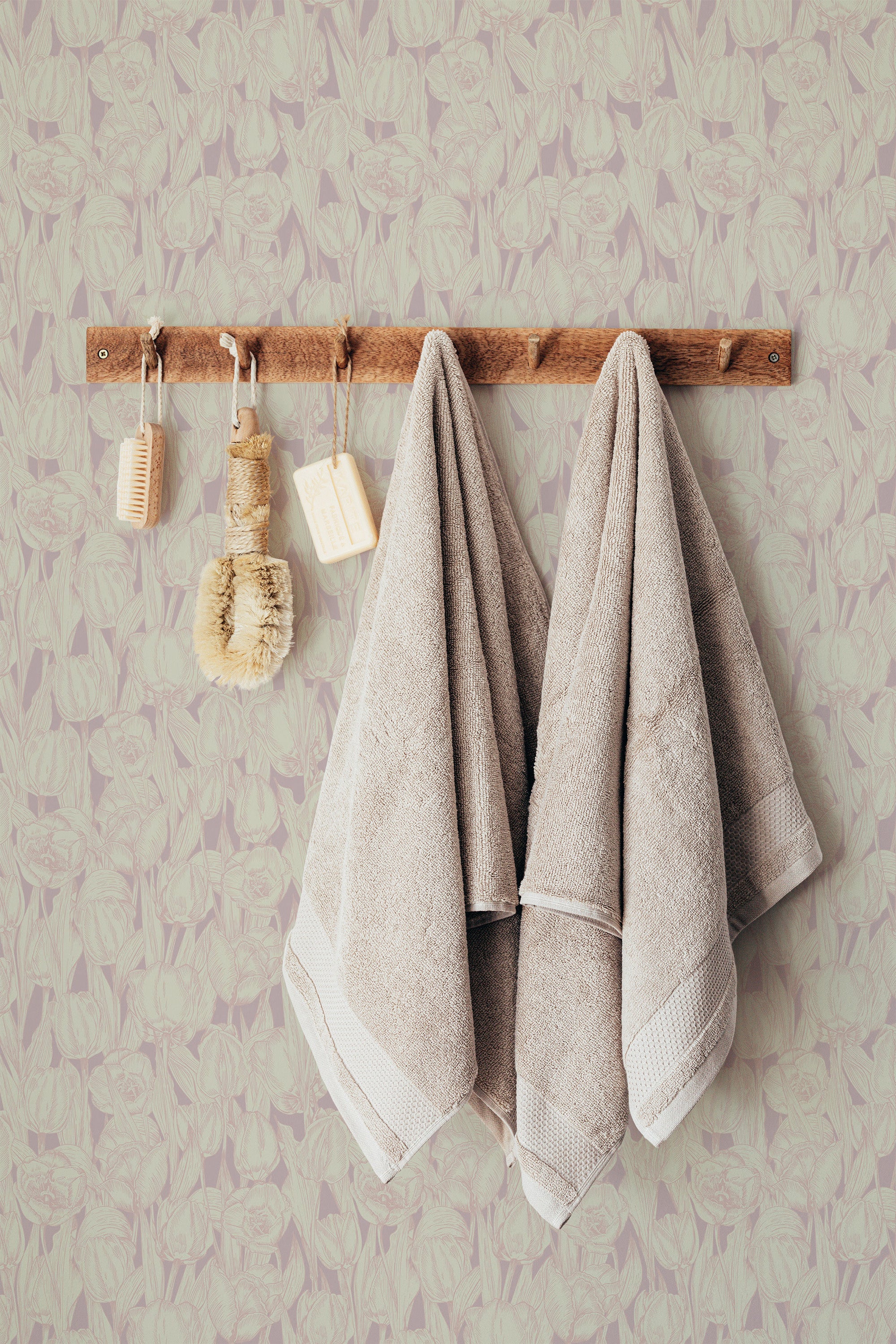Self-adhesive pink tulip wallpaper with a subtle floral pattern behind a wooden rack holding two beige towels and bath brushes.