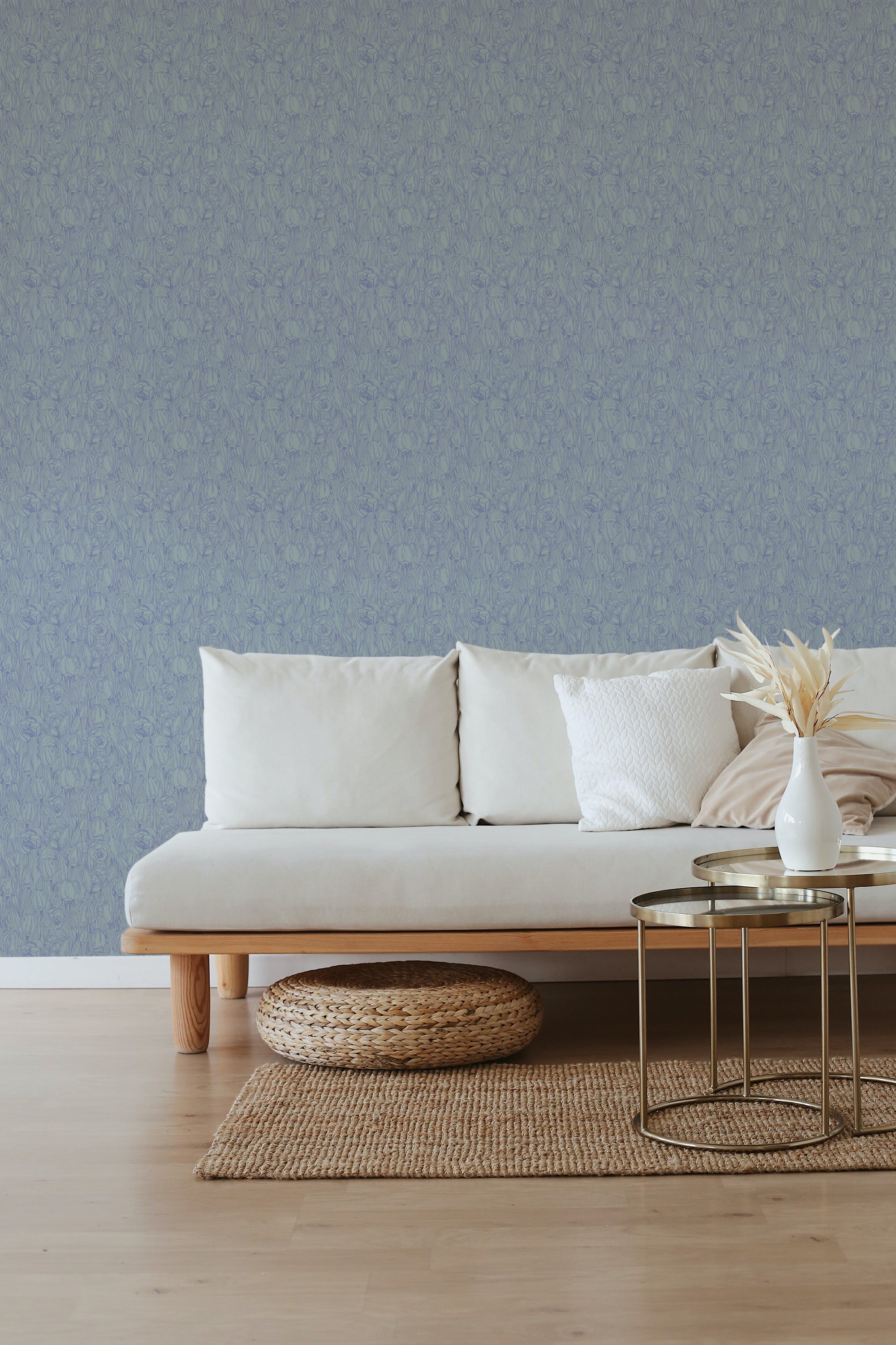 A serene room with a wall covered in blue tulip-patterned wallpaper, giving a classic and elegant ambiance, accompanied by a cream sofa, a natural woven ottoman, and a small metallic coffee table, embodying traditional wallpaper.