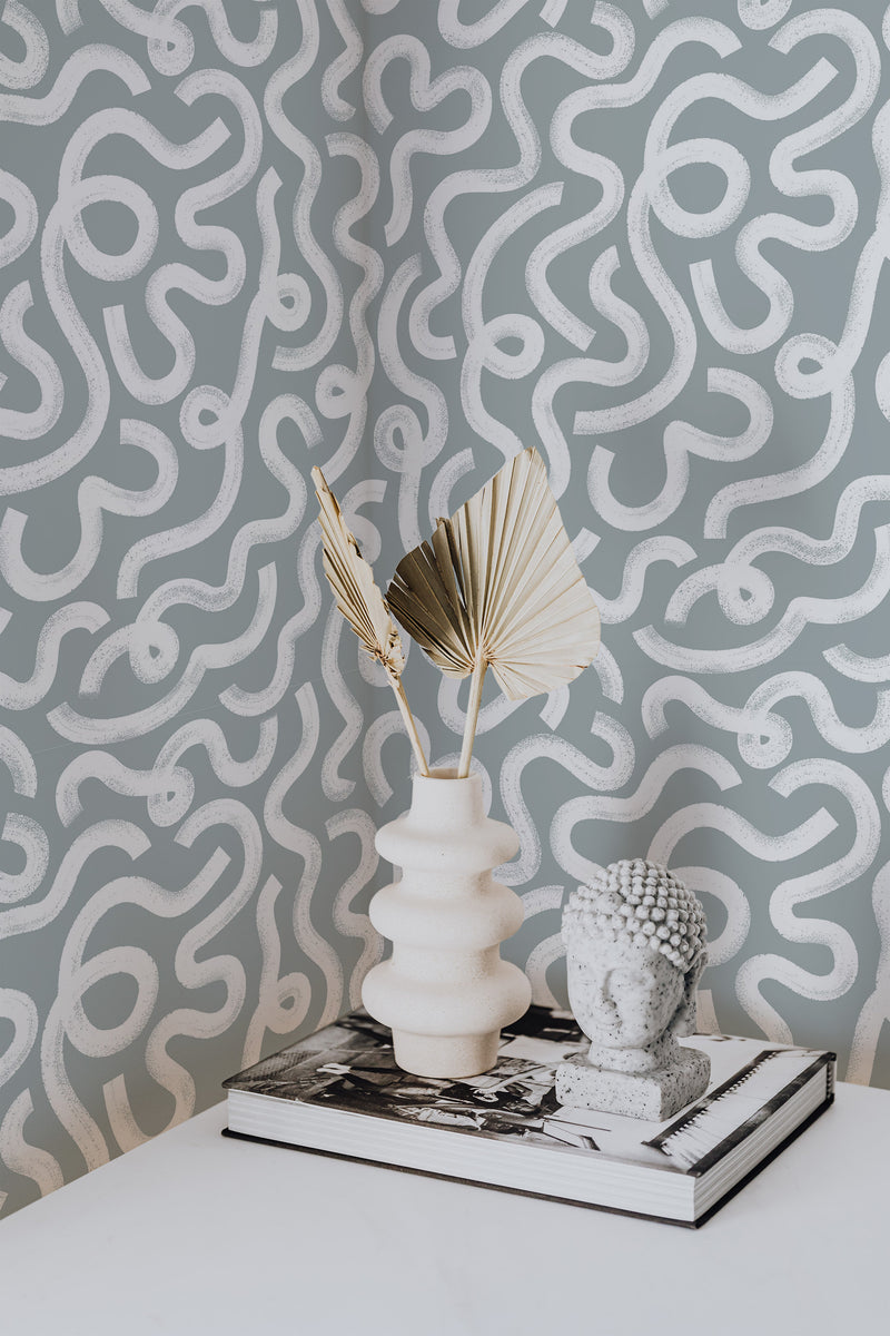 Self-adhesive wallpaper with abstract rainstorm brush line pattern in shades of gray and white, accentuated by modern decorative objects.