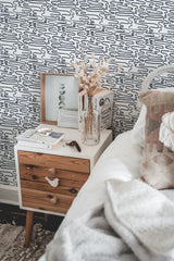 Self-adhesive wallpaper with a Lined Brush design in a room, showcasing abstract black lines on a white background, with a side table and bed in the foreground.