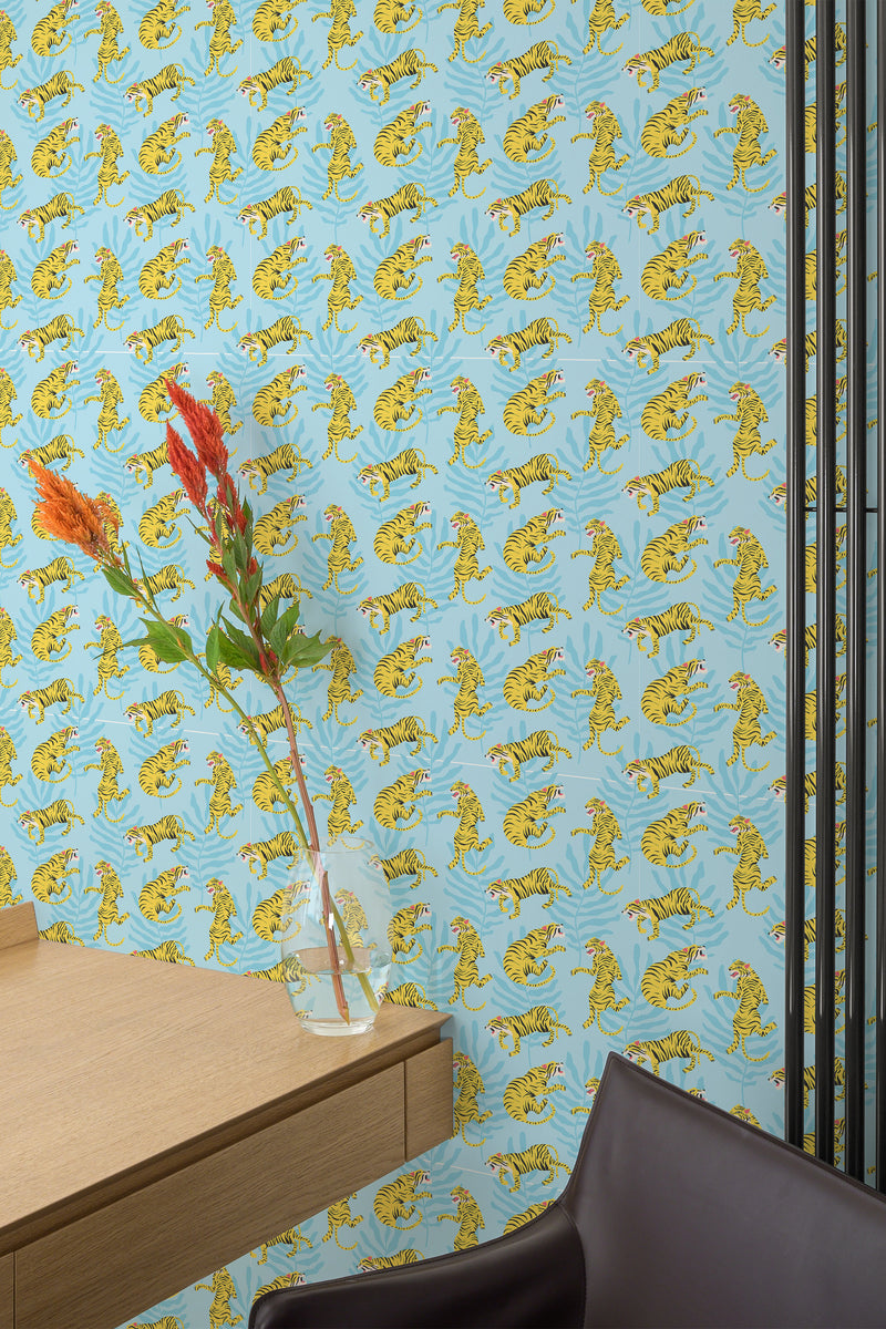 Self-adhesive wallpaper with a bold pattern of yellow tigers on a blue background in a room with a wooden desk and a vase with flowers.