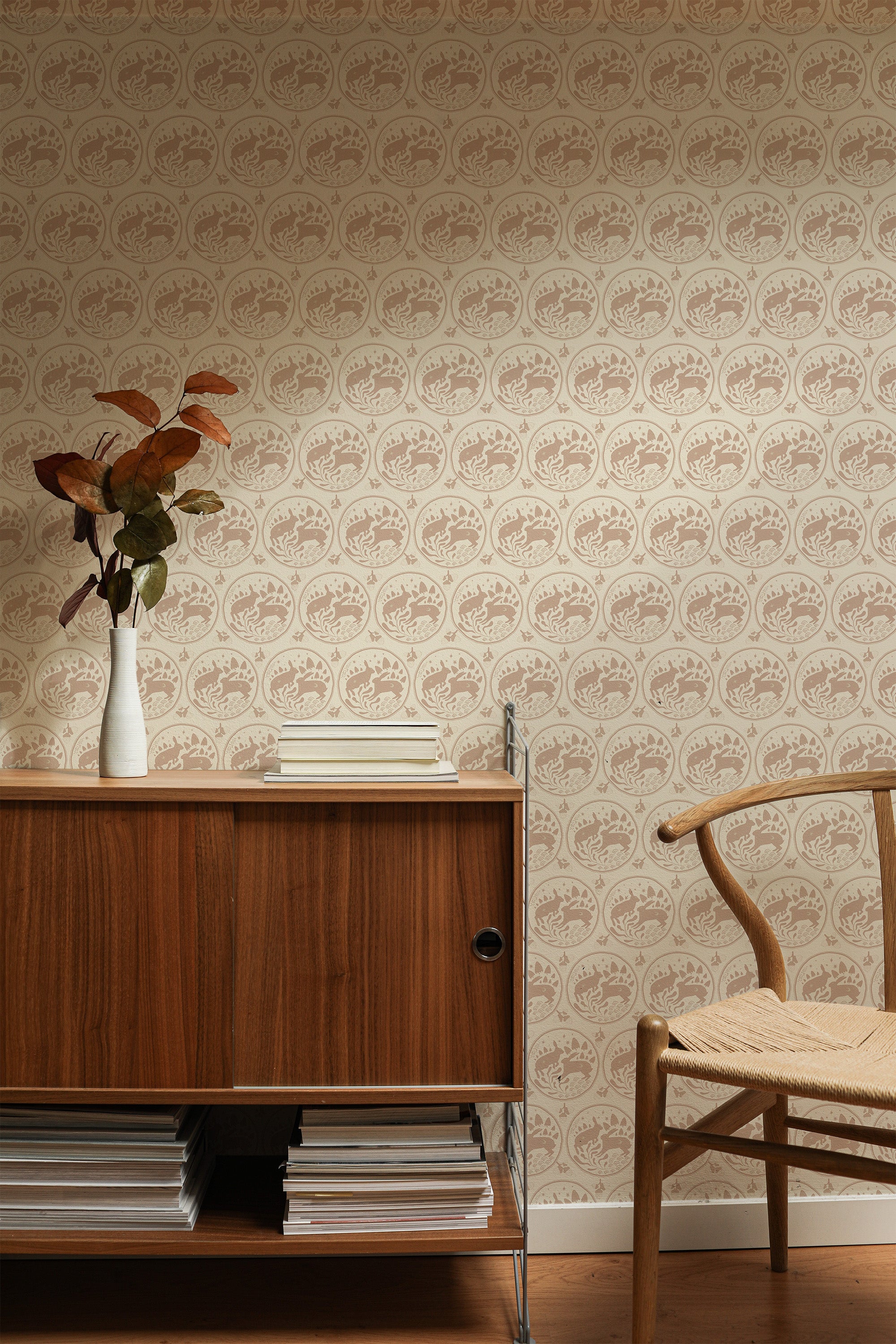 Self-adhesive Vintage Rabbit wallpaper with a repeated pattern of rabbits within ornate frames on a beige background, behind wooden furniture.