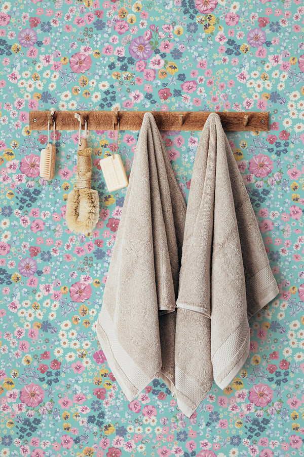 Self-adhesive wallpaper with a Flowers On Blue design, including various colorful floral patterns on a light blue background, with hanging towels and bathroom accessories in the foreground.