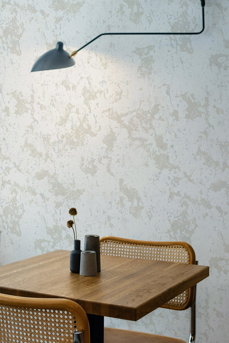 Self-adhesive limewash pattern wallpaper with a distressed look, in neutral tones on a room's wall above a wooden table with a vase and dried flowers.