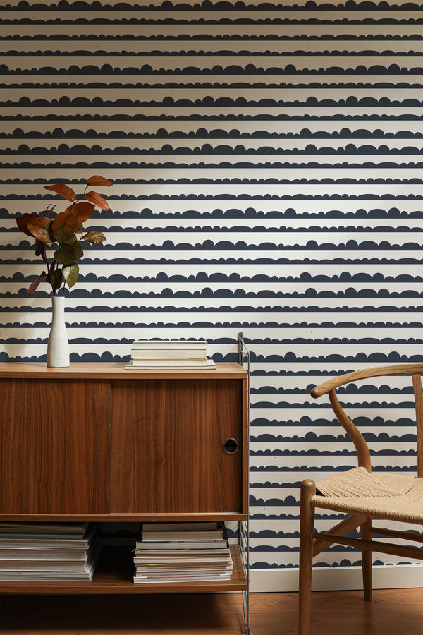 Self-adhesive wallpaper with a repeating wavy pattern resembling stylized clouds in dark and light hues on a room wall, complemented by wooden furniture.