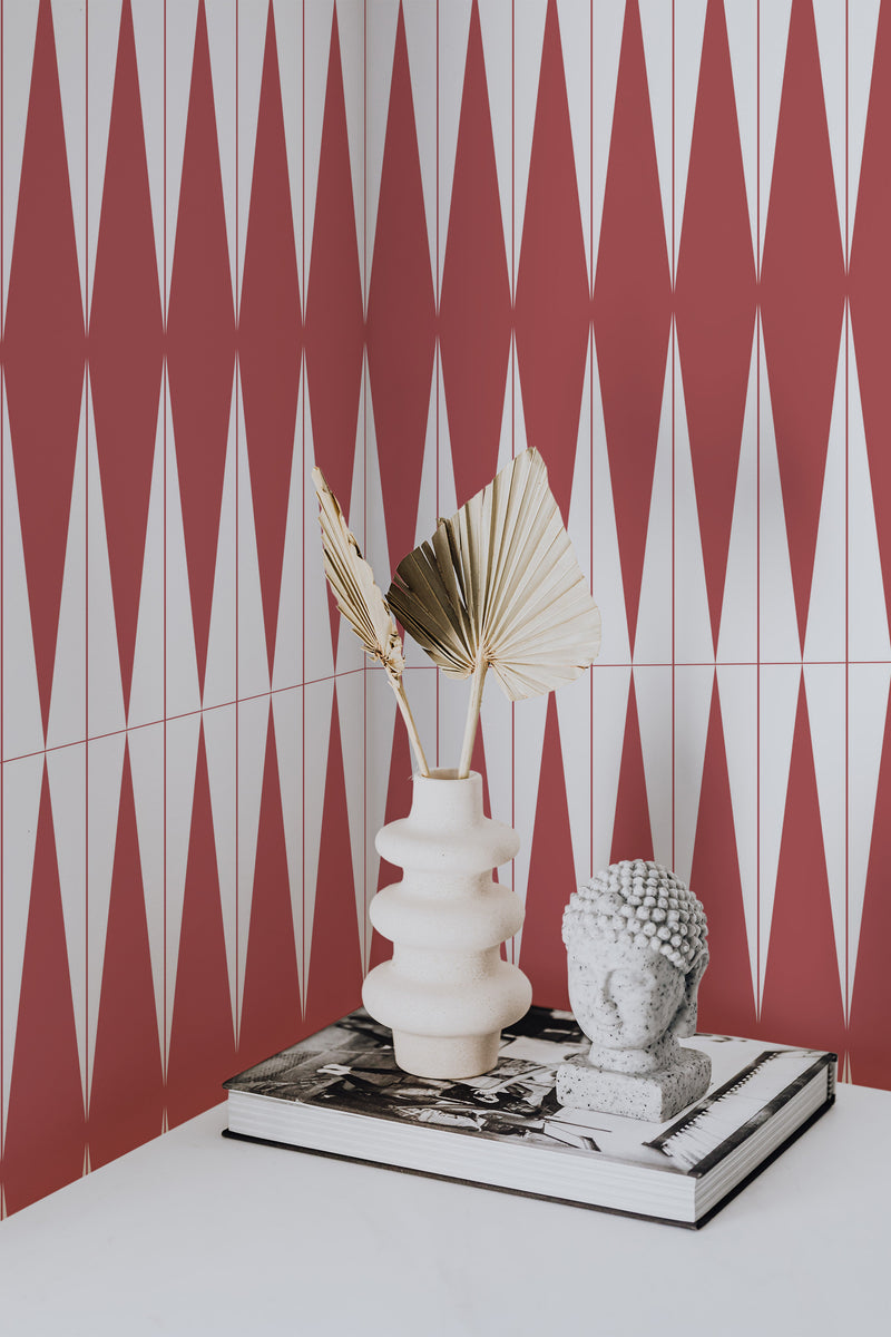 Self-adhesive Bold Slim Harlequin wallpaper with alternating red and white vertical zigzag stripes on a wall in a room, accompanied by a decorative vase and objects on a tabletop.