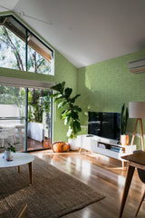 A room with one wall covered in Green Vintage Leaves wallpaper with a subtle leafy pattern, complementing the natural light and modern furnishings, traditional wallpaper.