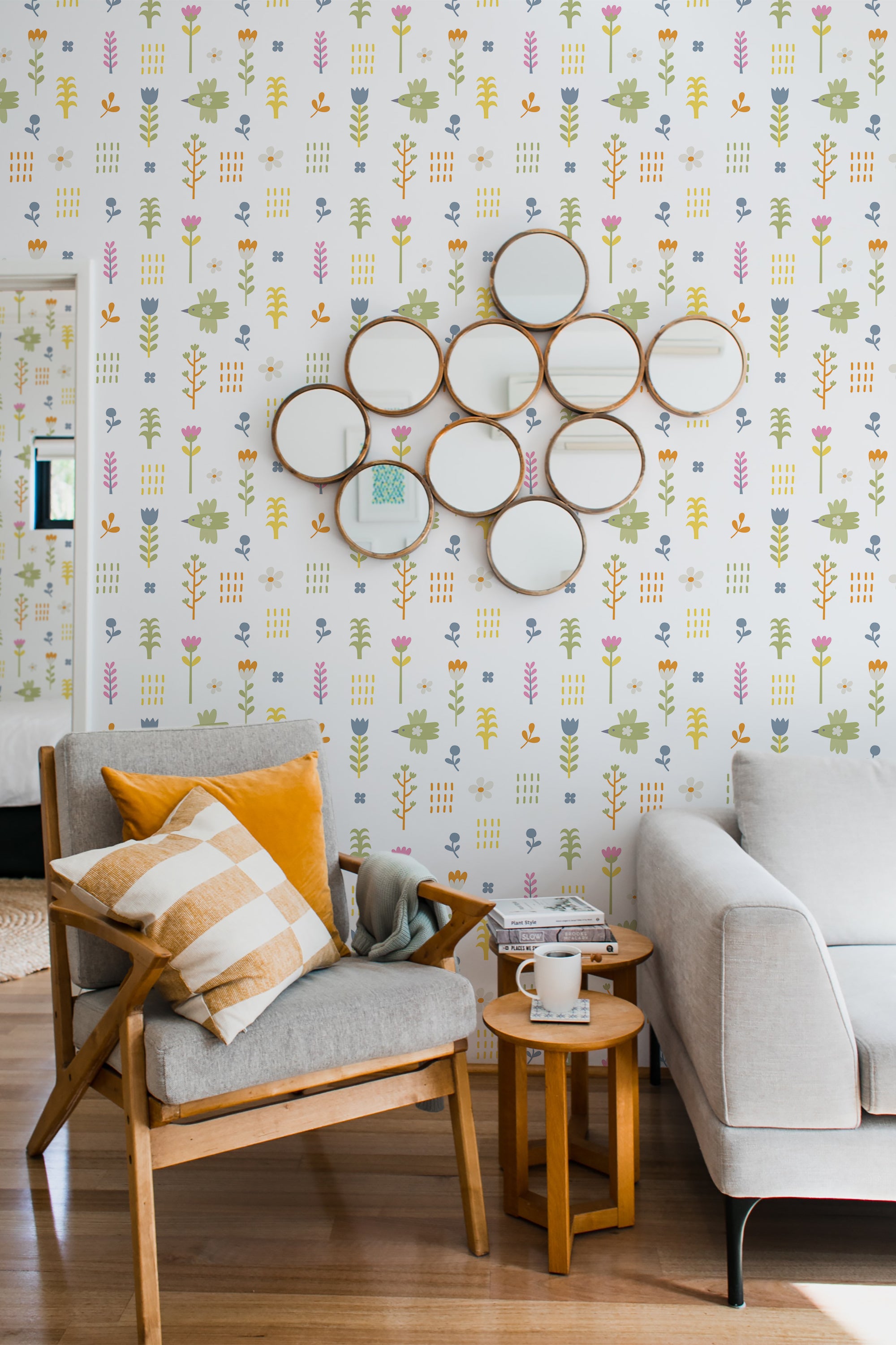 A bright room with Cute Birdie wallpaper pattern, showing colorful birds and foliage on a creamy background, complemented by a wooden armchair and a sofa, adhering to a traditional wallpaper style.