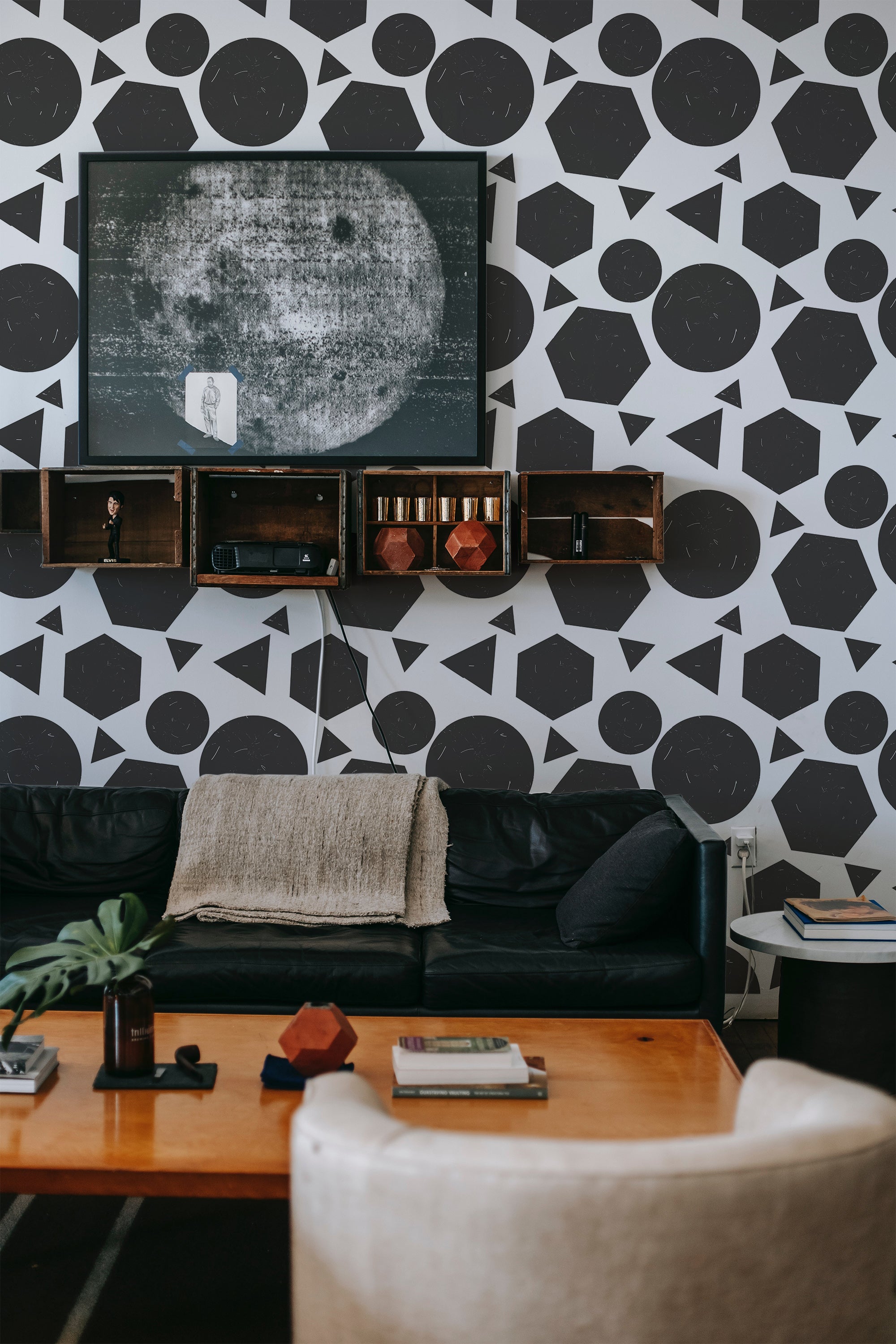 A living room with a wall covered in geometric-patterned wallpaper, including large circles and half-circles in a repeating dark and white motif, above a black leather sofa, traditional wallpaper.